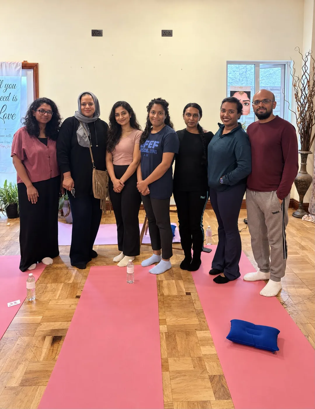 Seven workshop participants and Sanja Joy posing together after a Guidance with Joy session in Wanstead, East London, standing on pink yoga mats