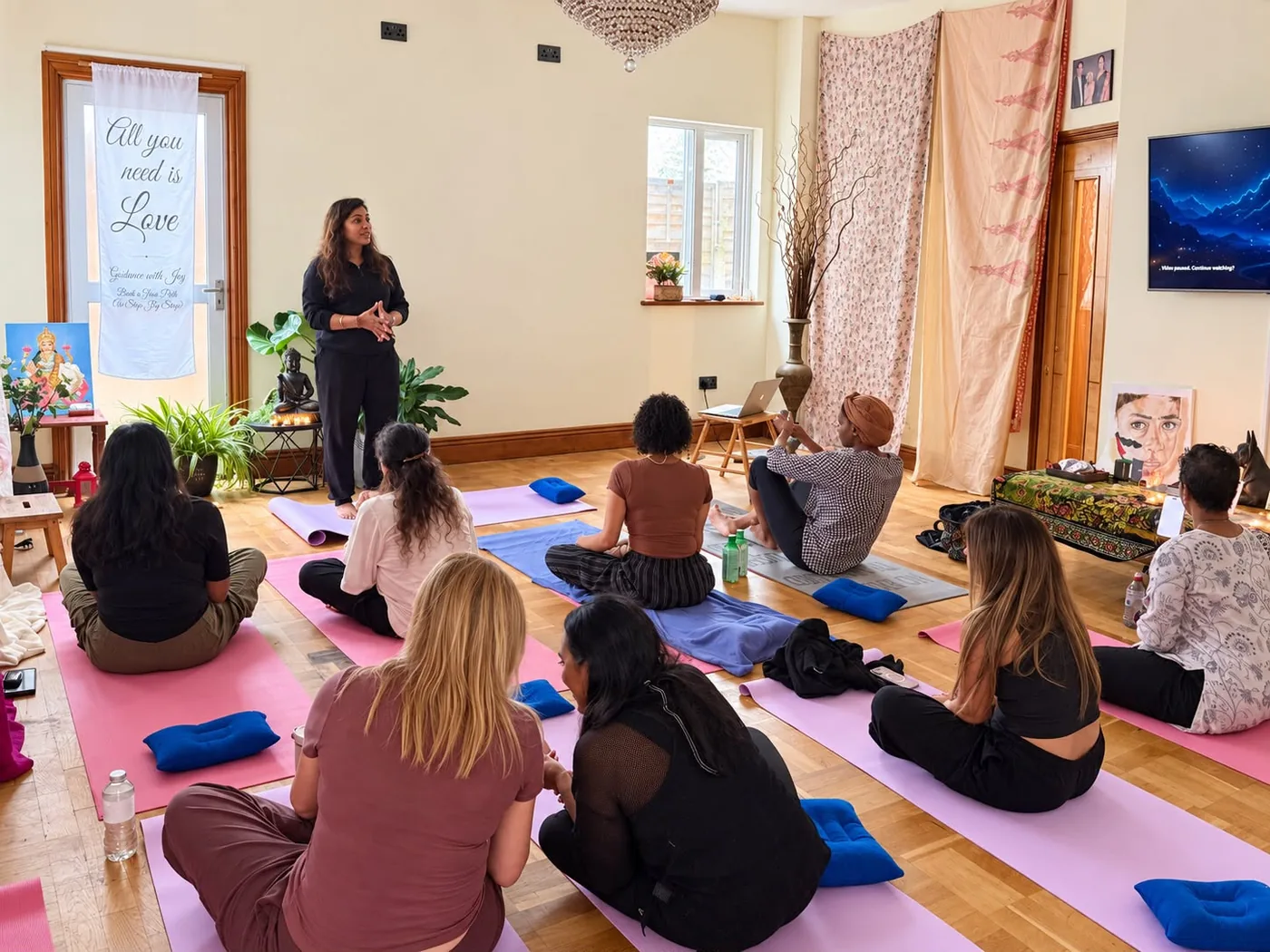 Sanja Joy leading a seated group meditation for workshop attendees on floor mats in a sunlit room